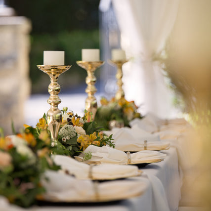 Party & Event RentalsElegant table setting with tall gold candleholders and white candles, surrounded by lush floral arrangements with yellow and orange blooms, exuding a festive, sophisticated ambiance.